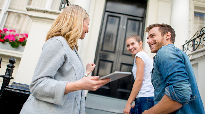 A young couple stand in front of home with realtor.