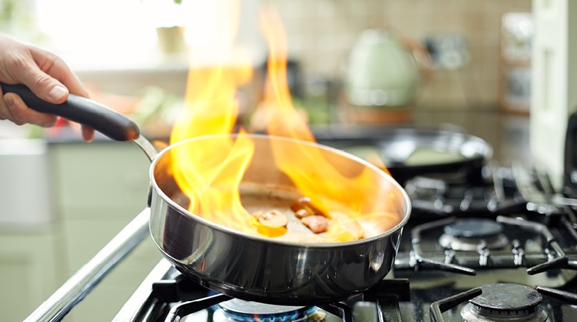 Someone cooking vegetables in a pan on fire on the stove.