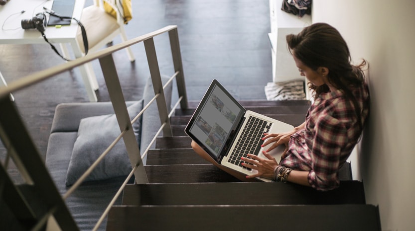 A woman sitting on the steps of her apartment working on a laptop.