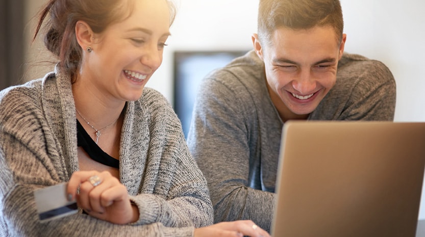 A young couple smiling at their laptop and holding a credit card.