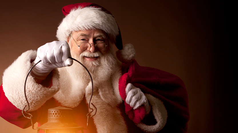 An old classic Santa Claus character stands smiling and holding a glowing lantern.