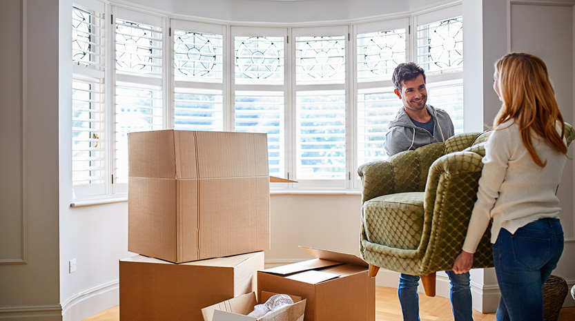 A man and woman carry a chair into a bright new living room.