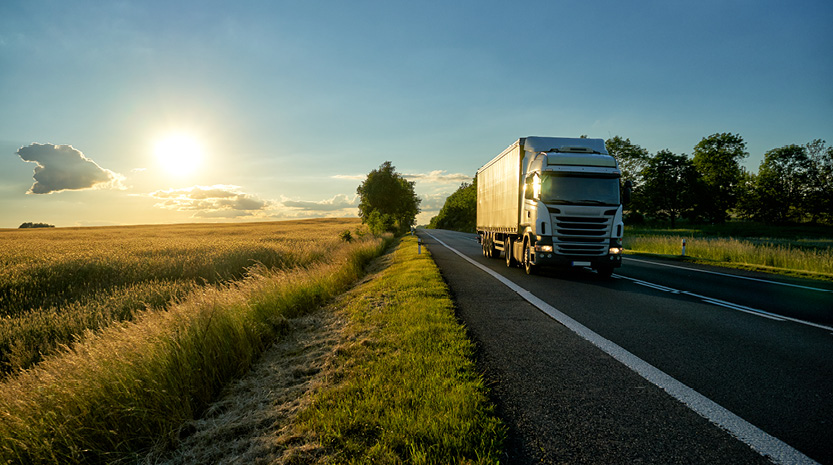 A large semi truck travels down a country road at sunset.